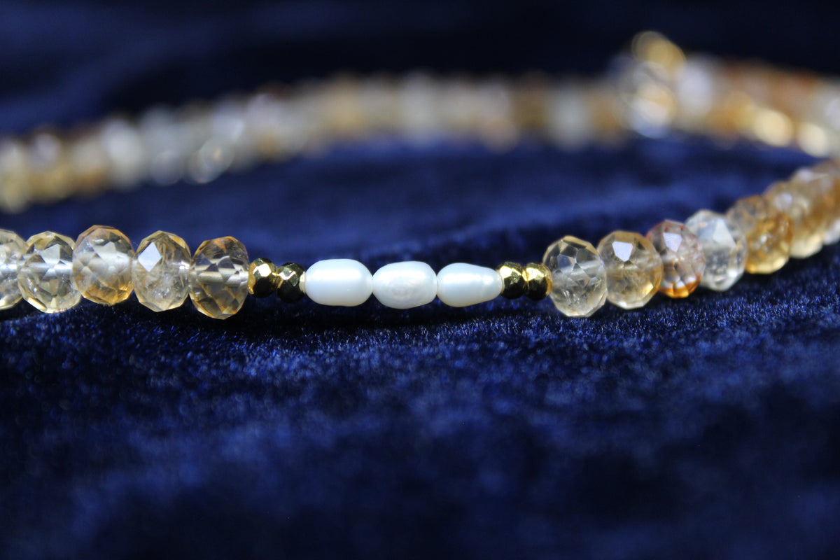 Necklace with faceted citrine beads, freshwater pearls, and gold hematite accents on a dark blue velvet background.
