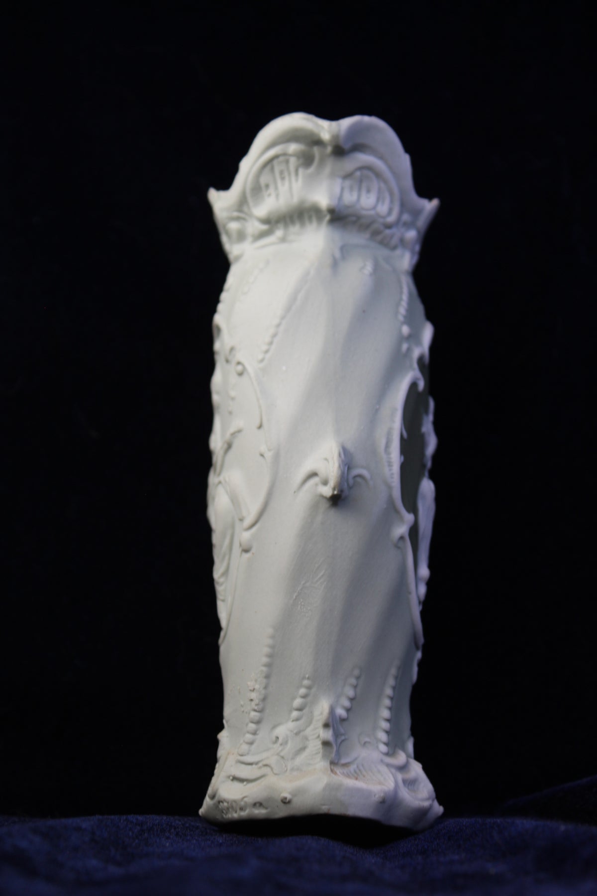 White Art Deco vase with intricate raised floral and scroll details, on a dark background.