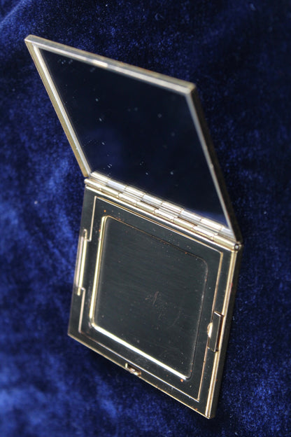 Gold-tone vintage compact with open mirror and empty powder compartment.
