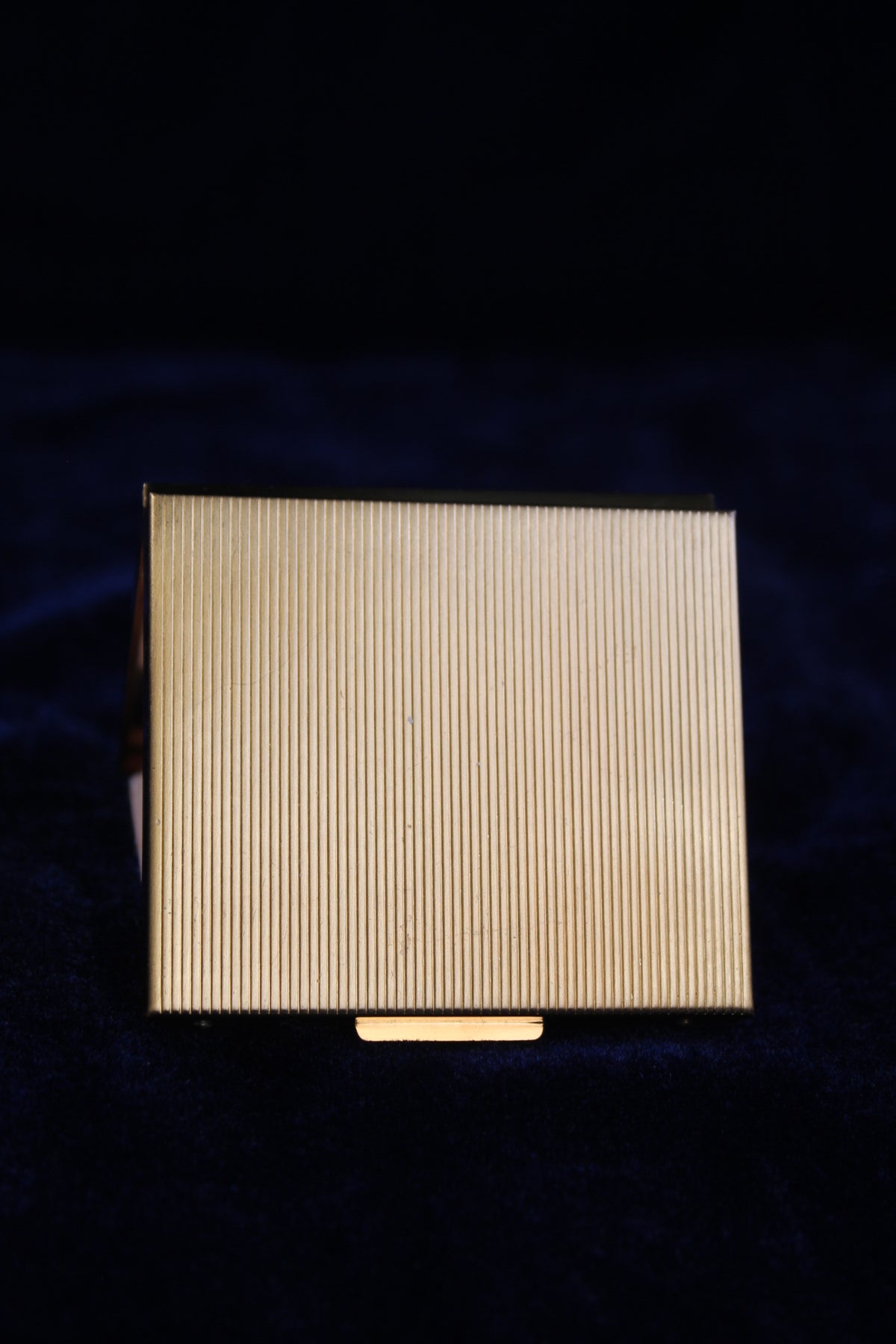 Gold-toned ribbed powder compact with a small latch on the bottom edge.