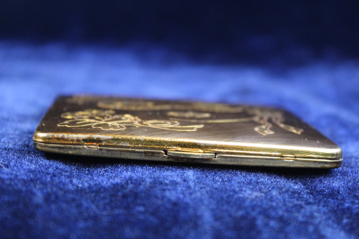 1940s gold tone vanity compact with engraved mask and floral motif.