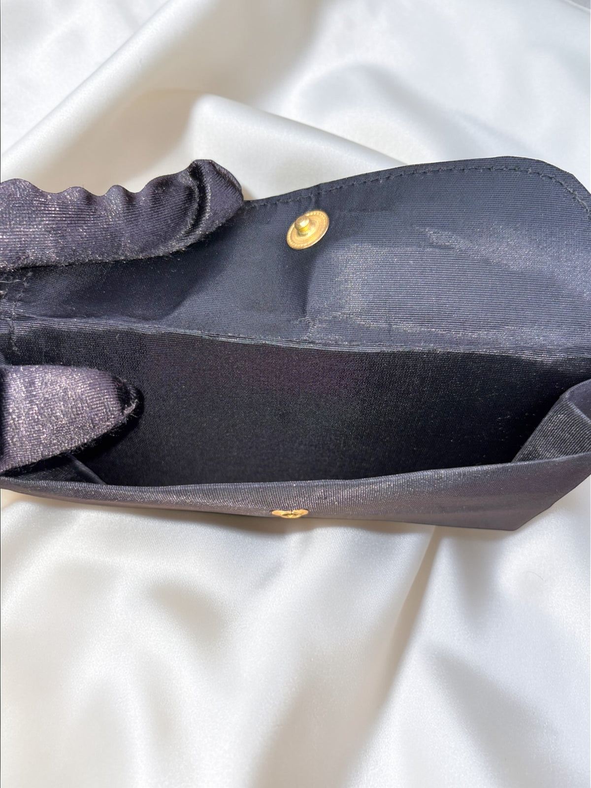 Interior of a black fabric clutch purse with a gold snap closure and a shimmering fabric lining.