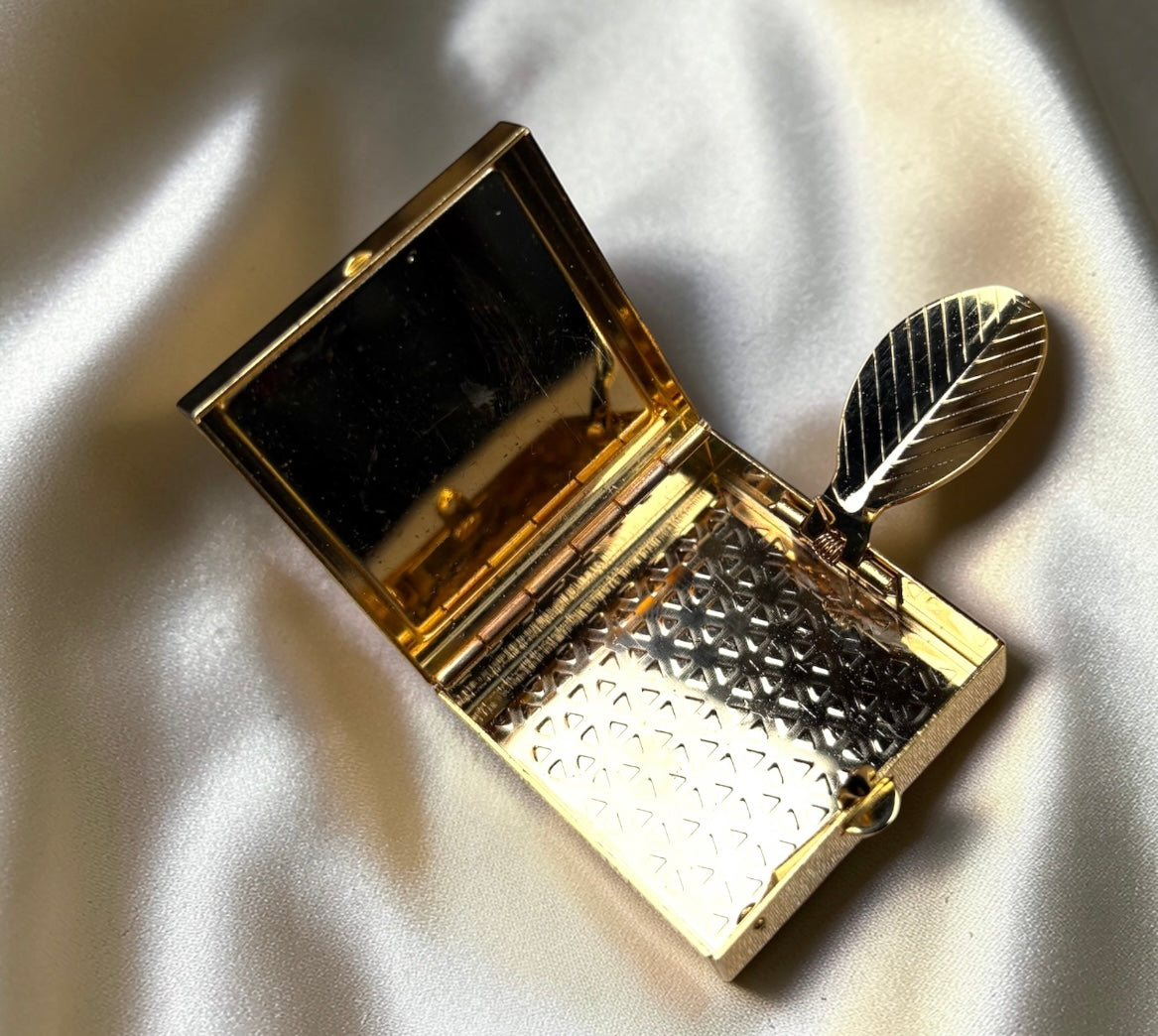 Gold-tone mini ashtray with leaf detail and patterned interior, open to show mirror.