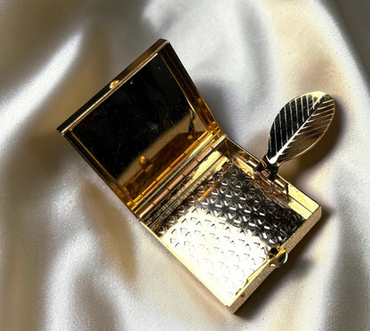 Gold-tone mini ashtray with leaf detail and patterned interior, open to show mirror.