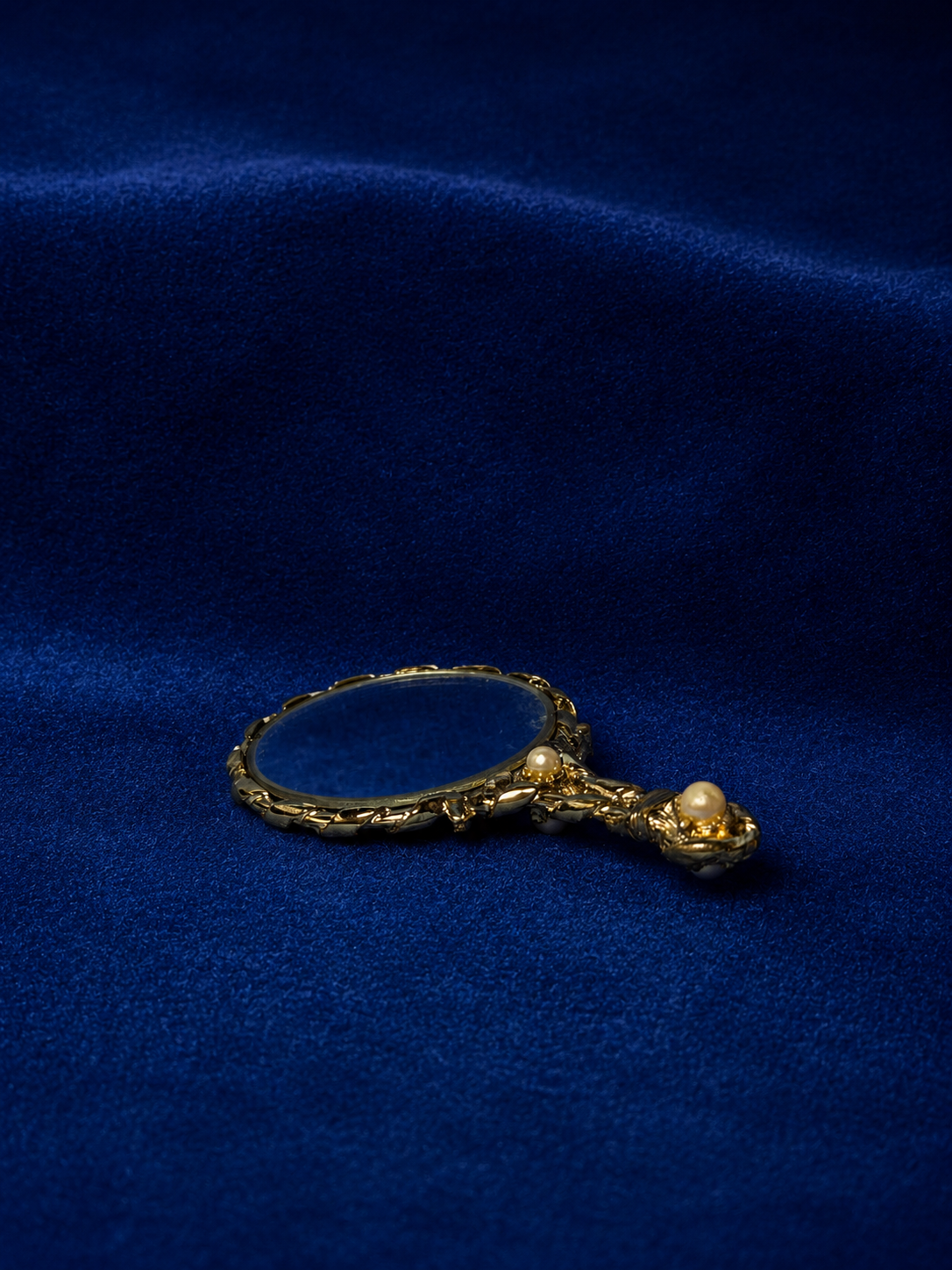 Gold-toned hand mirror with pearl accents on a blue velvet background.