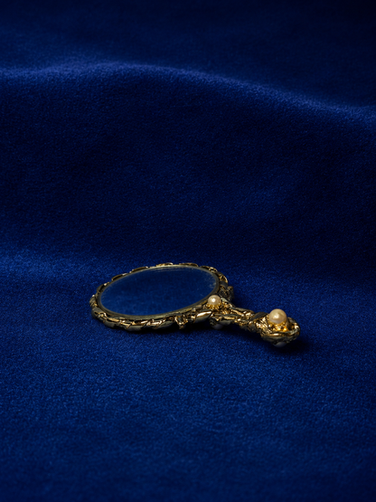 Gold-toned hand mirror with pearl accents on a blue velvet background.