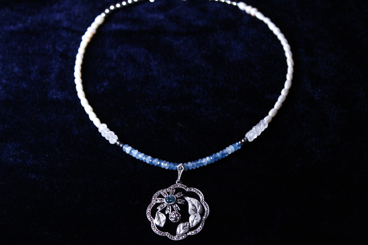 Sterling silver pendant necklace with aquamarine and moonstone beads on a dark blue background.