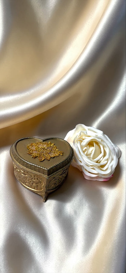 Vintage heart-shaped brass jewelry box with gold floral design and a white rose on a satin background.