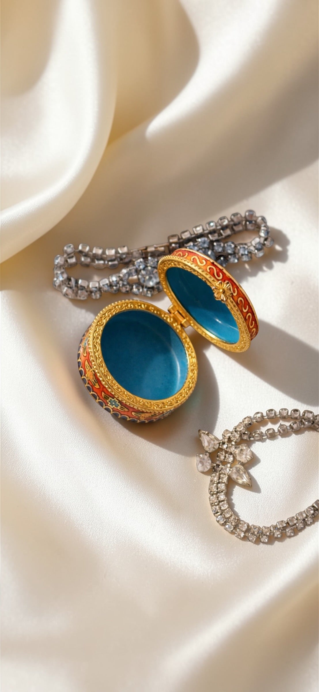 Orange red enamel cloisonné butterfly trinket box with blue interior, next to two rhinestone bracelets.