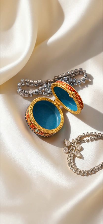 Orange red enamel cloisonné butterfly trinket box with blue interior, next to two rhinestone bracelets.