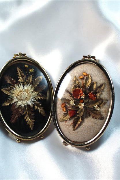 Two oval vintage frames with pressed flowers. One has white flowers on black, the other has orange flowers on beige.