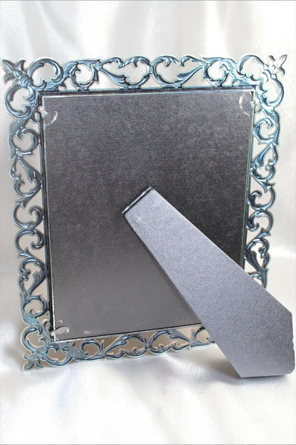 Back of a vintage metal picture frame with ornate baroque floral detailing and a gray easel stand.