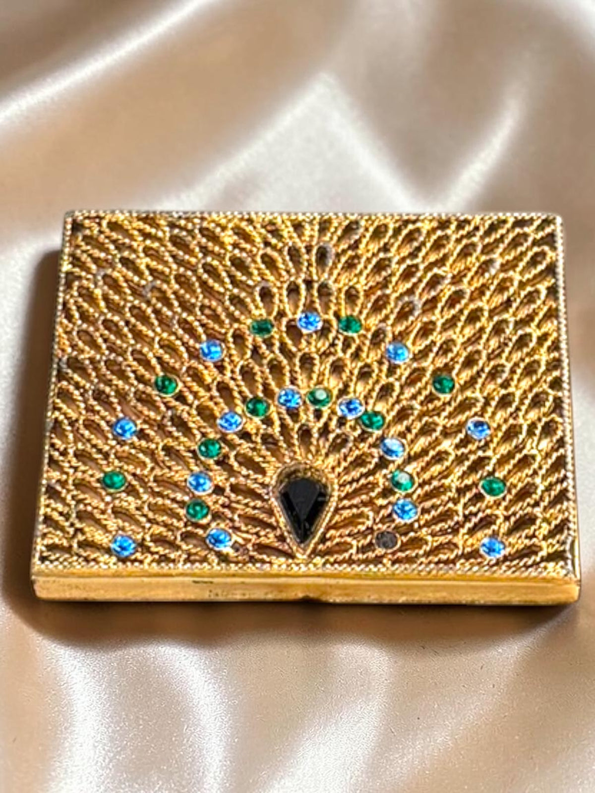 1940s gold-tone compact with ornate peacock filigree, blue and green rhinestones, and a black teardrop stone.