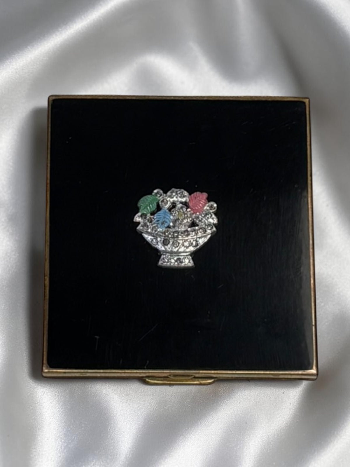 1940s black enamel compact with a silver floral basket motif featuring colorful flowers and leaves.