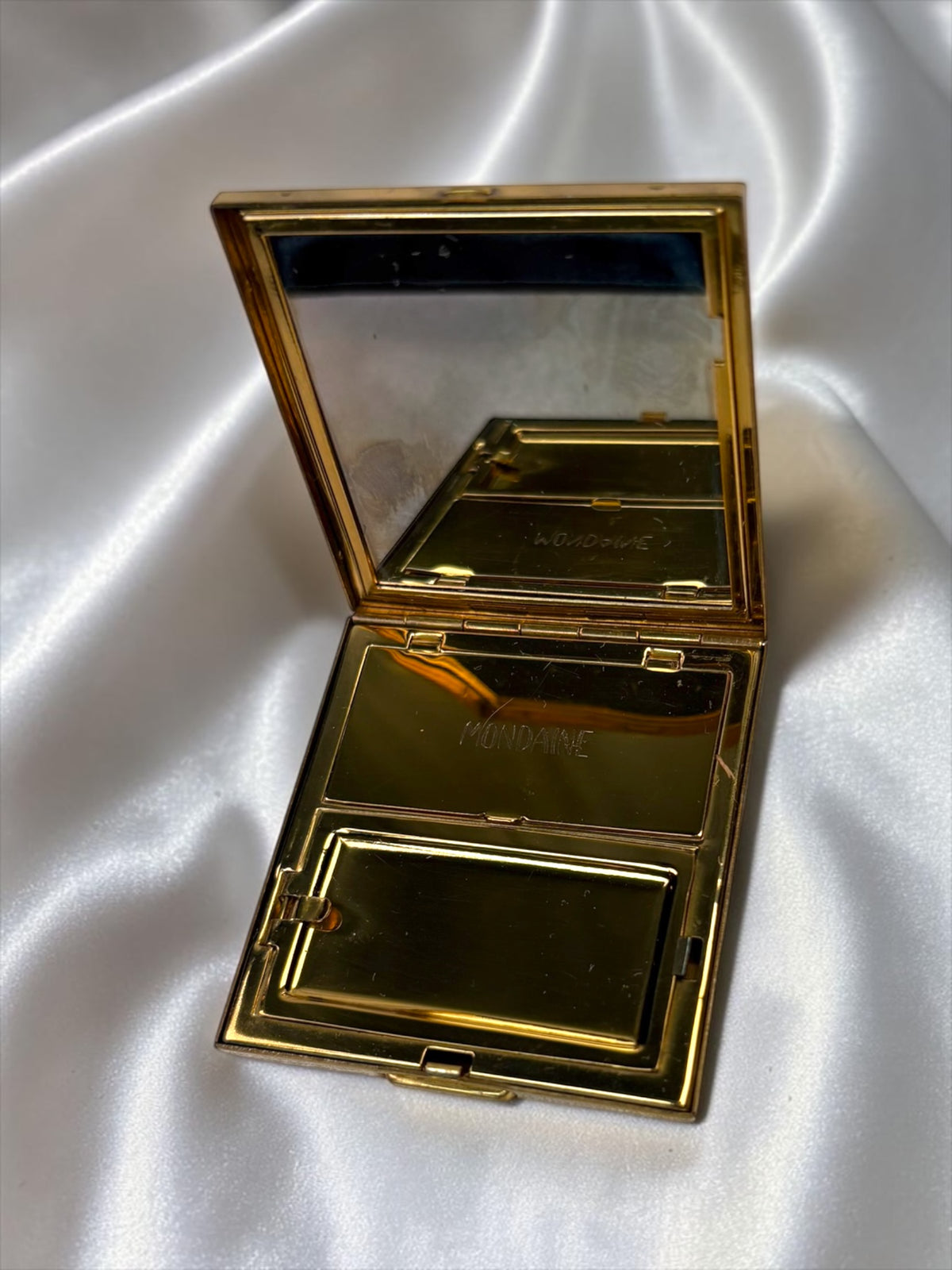 Gold compact with mirror open, showing the "MONDAINE" logo inside.