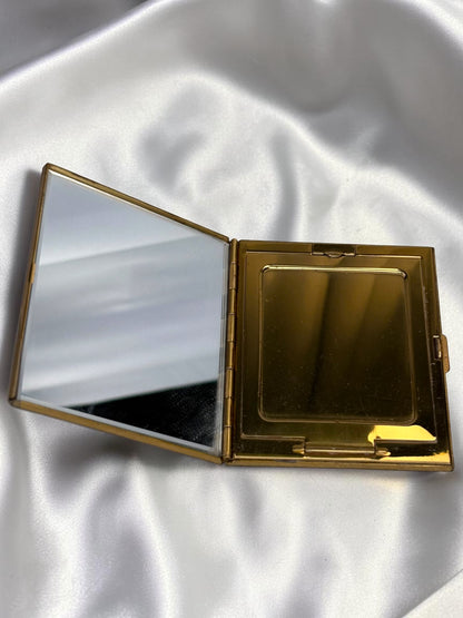 Open gold compact with a mirror on the left and a powder compartment on the right, on a white satin background.