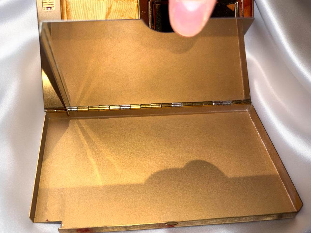 The interior of a vintage gold-tone Volupte carryall compact featuring a hinged mirror and open compartment.