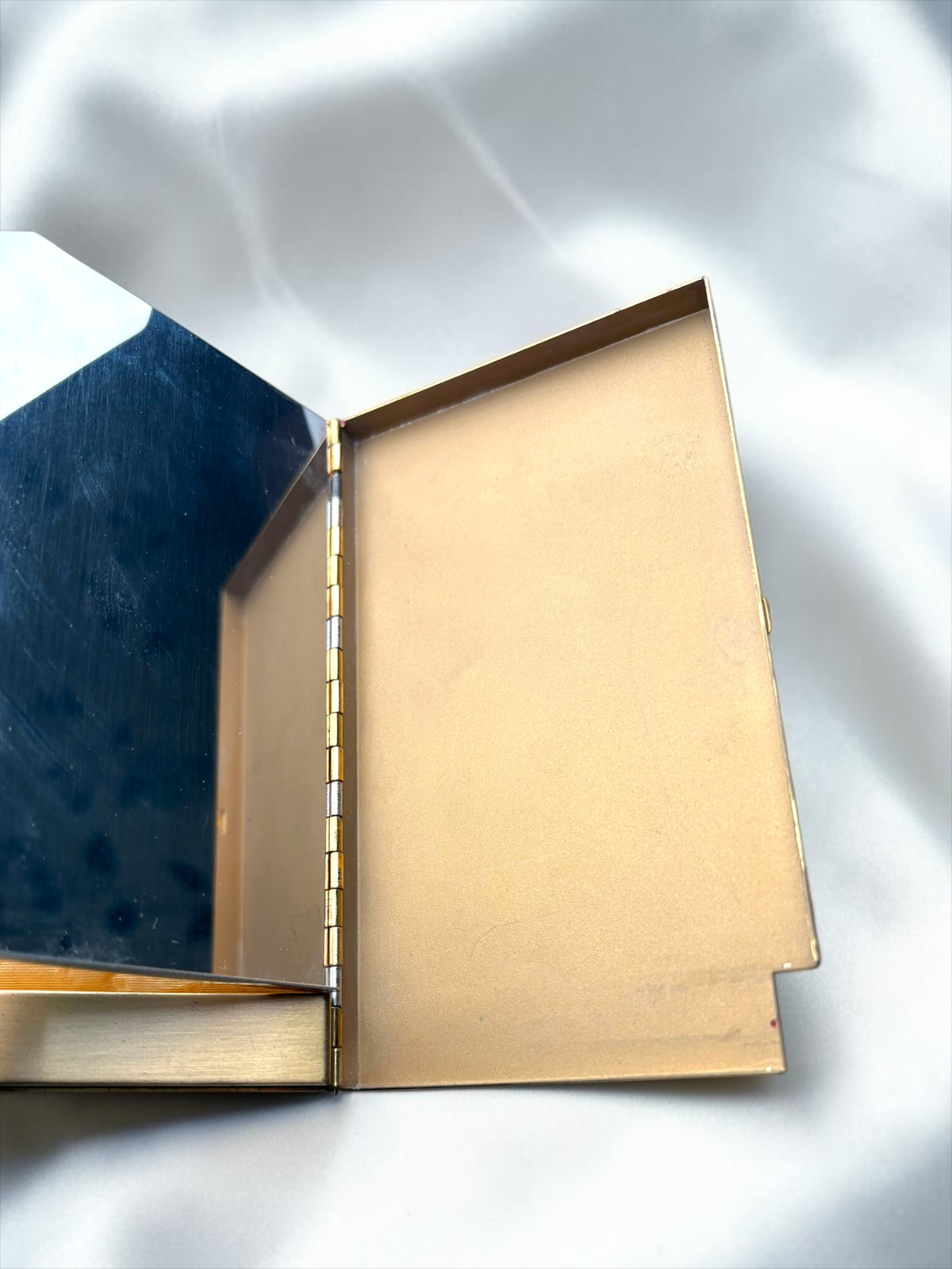 Open vintage gold-toned compact with a mirror on the left and a compartment on the right.