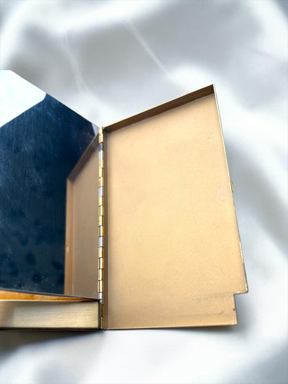 Open vintage gold-toned compact with a mirror on the left and a compartment on the right.